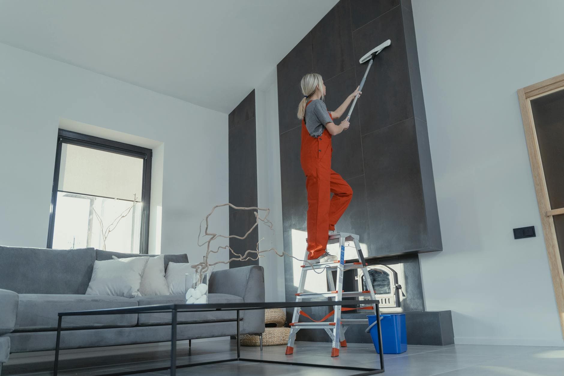 Pennsylvania Maid cleaner in red overalls on a ladder cleaning a high wall in a Pennsylvania apartment — Office Cleaning in Center City, Philadelphia