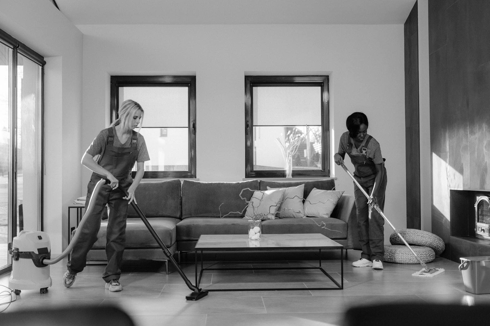Two Pennsylvania Maid cleaners in work uniforms using a vacuum and mop in a modern Pennsylvania living room — Office Cleaning in Fishtown, Philadelphia
