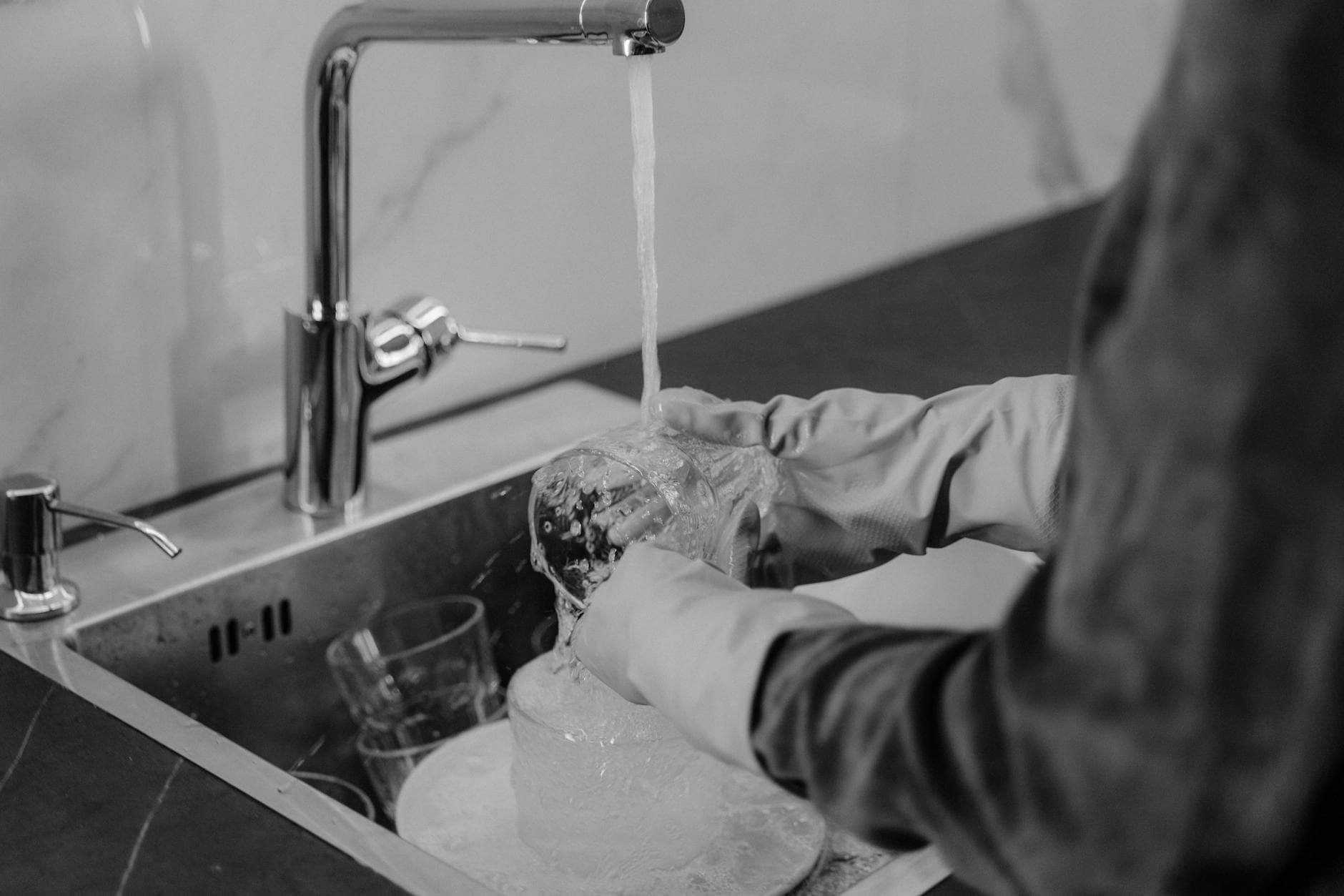 Pennsylvania kitchen cleaning service washing dishes under running water at the sink — Deep Cleaning in Pennsylvania